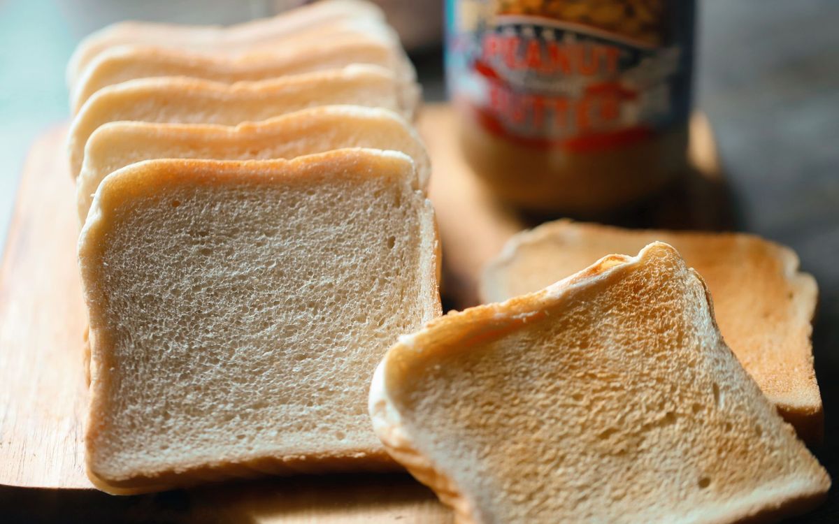 Slices of soft white sandwich bread from a basic white bread recipe on a wooden board.