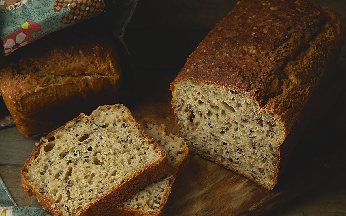 Whole wheat bread loaf with slices on a rustic wooden board, showcasing artisanal baking.